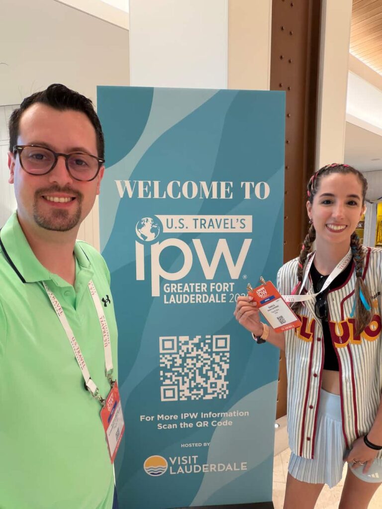 Casal posa sorrindo com credenciais em frente ao totem do "Bem vindos a IPW"