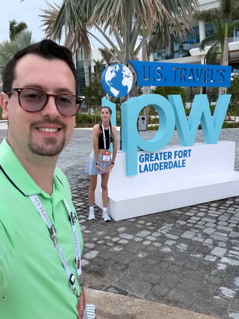 Casal posa sorridente em frente ao letreiro comemorativo da U.S. Travel IPW em Fort Lauderdale, evento de turismo para promover os Estados Unidos para o mundo
