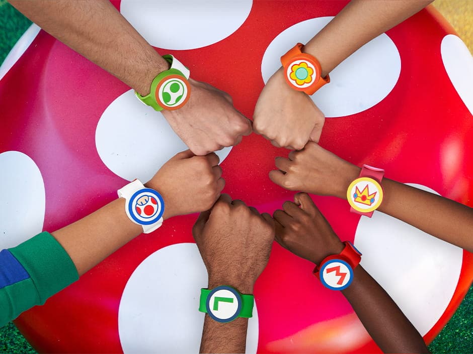 Grupo de amigos junta seus punhos ao centro em círculo mostrando que estão prontos para um dia de diversões com suas Power Up Bands dos personagens clássicos de Nintendo