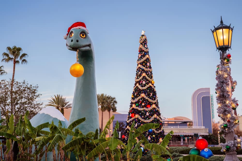 Gertie no Disney's Hollywood Studios segura uma bola de natal em sua boca bem perto da árvore de natal do parque