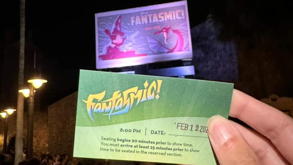 Imagem mostra pessoa segurando o voucher do Fantasmic Dining Package em frente ao Outdoor do show noturno do Disney's Hollywood Studios em Walt Disney World Resort