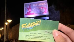 Imagem mostra pessoa segurando o voucher do Fantasmic Dining Package em frente ao Outdoor do show noturno do Disney's Hollywood Studios em Walt Disney World Resort