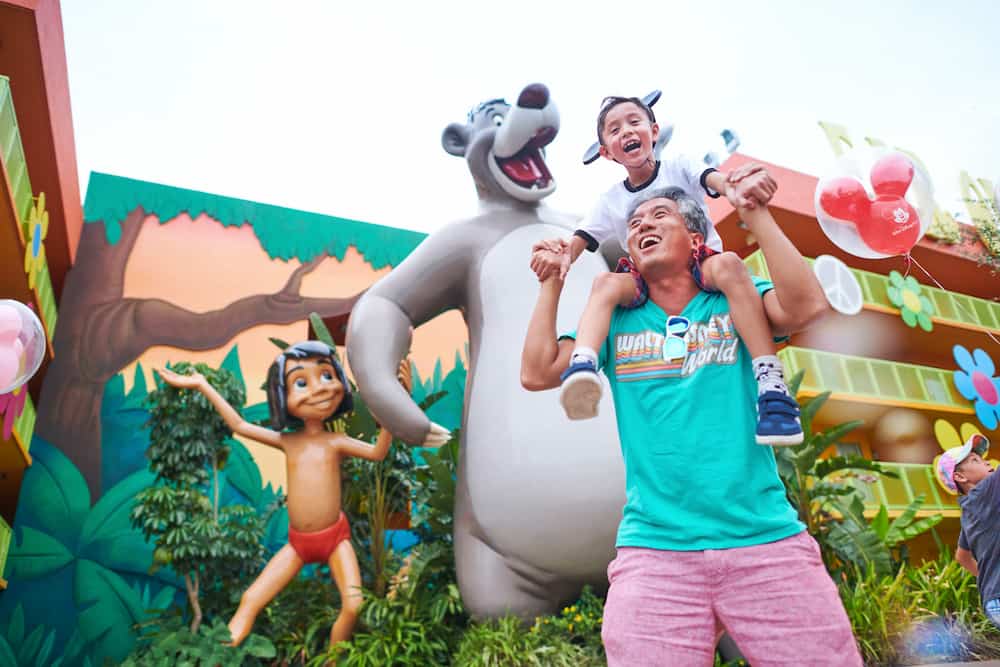 Pai leva seu filho nos ombros em frente a Mowgli e Baloo no Disney's Pop Century Resort