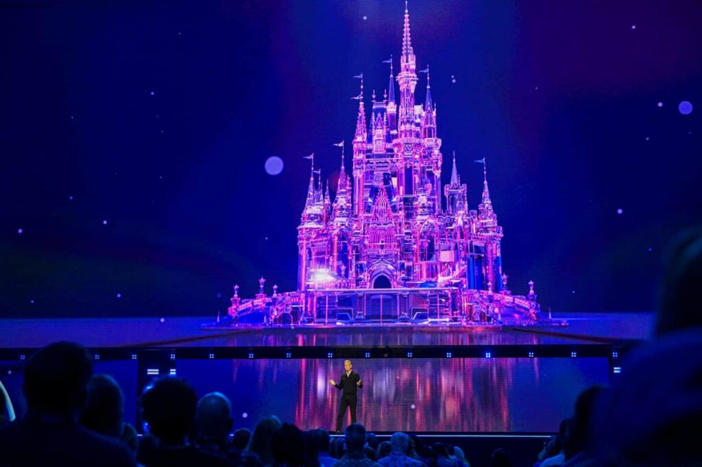 Josh Damaro em frente ao telão com um lindo castelo da Disney durante anúncios de filmes e streaming da D23 2026
