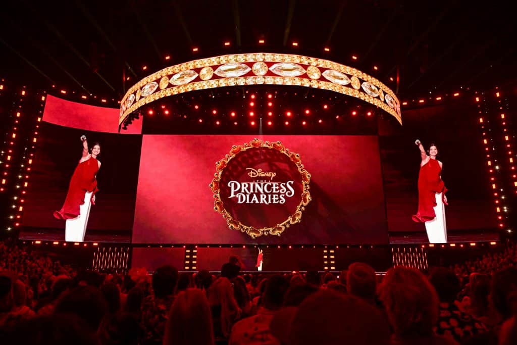 Anne Hathaway anuncia Diários de uma Princesa 3 em frente ao poster projetado no telão na D23 2026