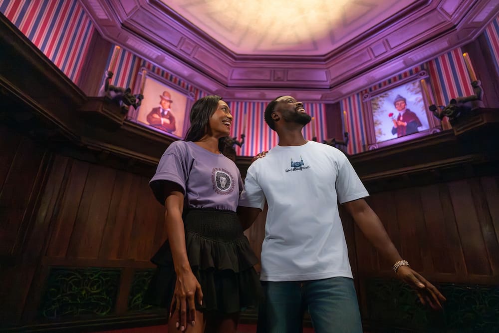 Casal dentro da atração da mansão assombrada enquanto usa roupas da coleção Haunted Mansion