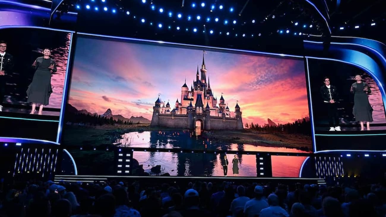 Grande telão com o castelo símbolo da abertura dos filmes Disney e pessoas assistindo ao painel de filmes e streaming da D23 2026