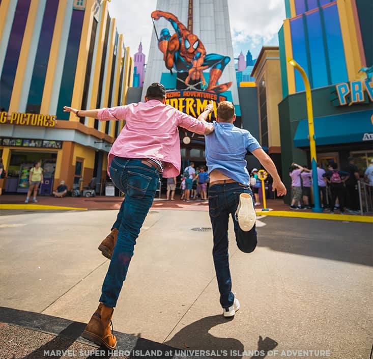 Pai e filho correm em direção a Atração do Homem Aranha - The Amazing Adventures of Spider Man no parque temático Islands of Adventure no Universal Orlando Resort