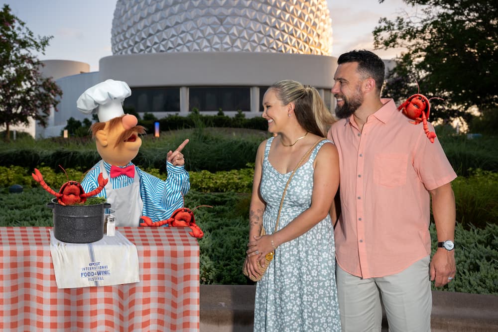 Casal posa com muppet chefe de cozinha e lagostas em magic shot do photopass no Epcot com a Spaceship Earth de fundo