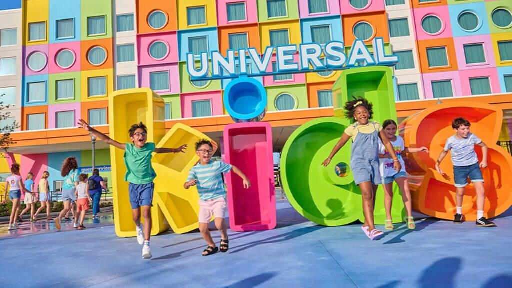 Fachada do hotel Universal Kids Resort em Frisco Texas, completamente colorido e vibrante, com as letras K - I - D - S em frente e crianças correndo e pulando felizes enquanto se divertem em Frisco no Texas