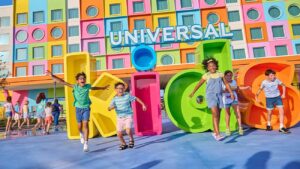 Fachada do hotel Universal Kids Resort em Frisco Texas, completamente colorido e vibrante, com as letras K - I - D - S em frente e crianças correndo e pulando felizes enquanto se divertem em Frisco no Texas