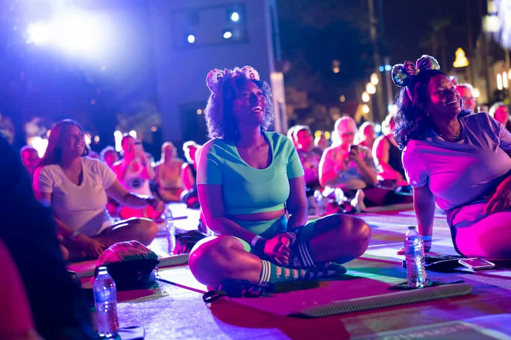 Pessoas se sentam de pernas cruzadas para participar das aulas de yoga oferecidas durante os eventos da runDisney