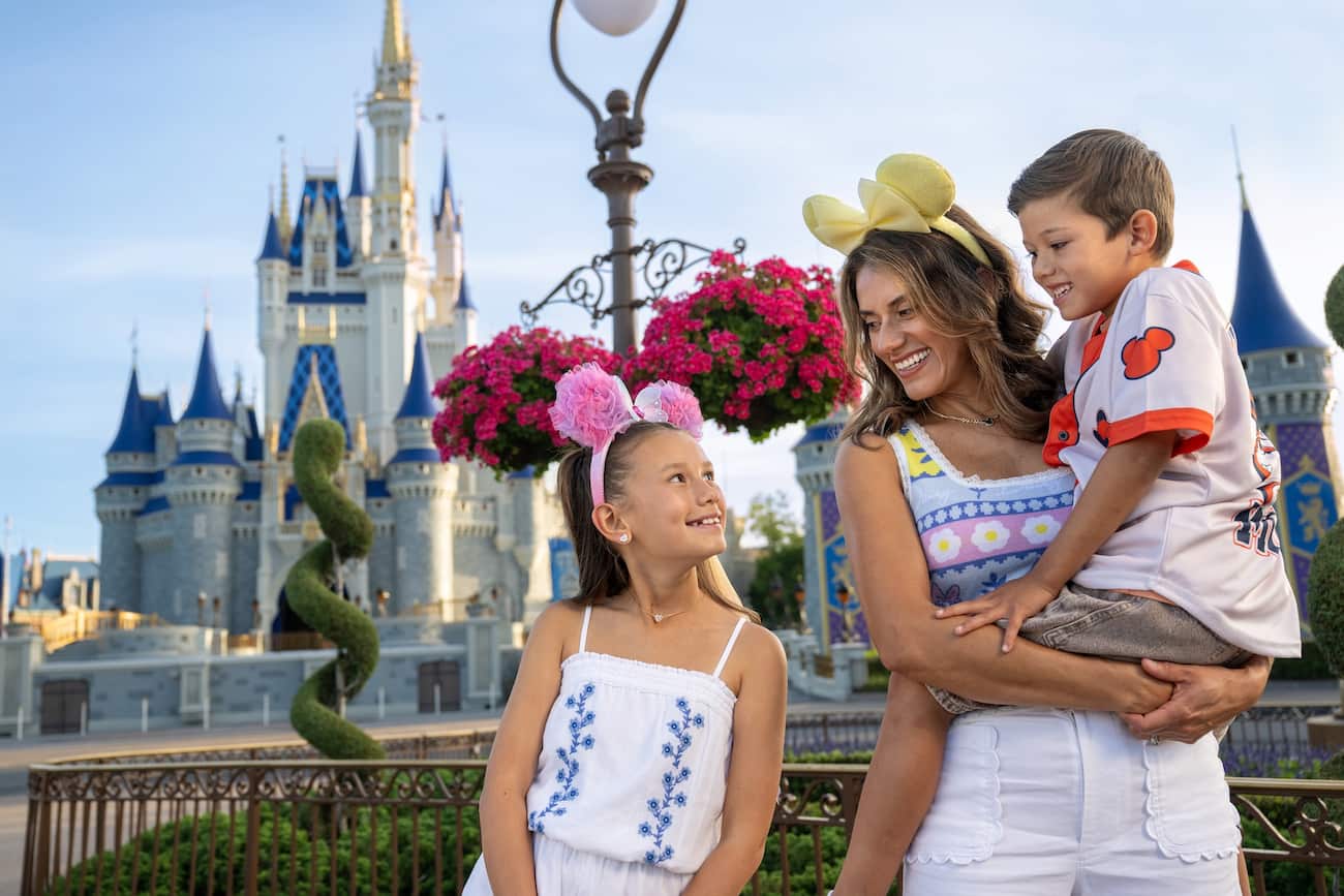 Mãe com seu filho no colo, olha e sorri pra outra filha que está ao seu lado, ambas usando orelhinhas da Minnie